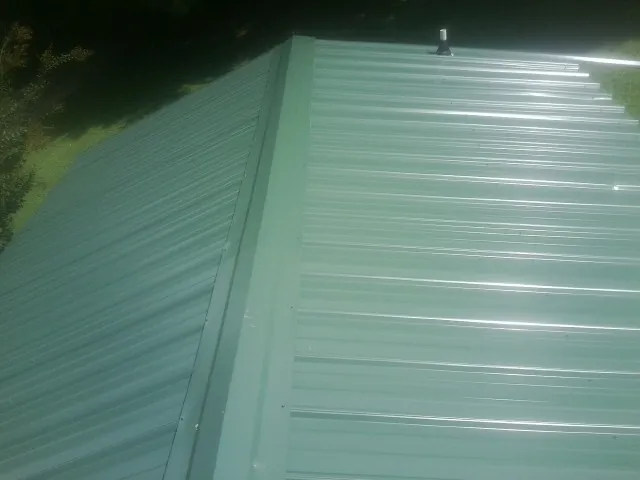 New green metal panels meeting at the ridge of a roof — Flat Roof Repair work by our crew in Trafford