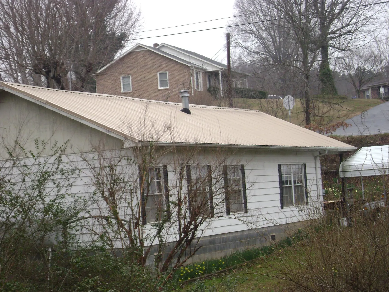 Tan metal roof on a white sided house set into a hillside — Commercial Roofing by Roofing Brothers in Trafford